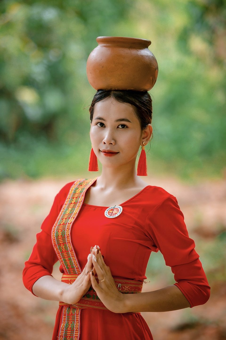 Cô gái dân tộc trong trang phục đỏ truyền thống đội ché trên đầu, chắp tay chào ở Suối Kiết